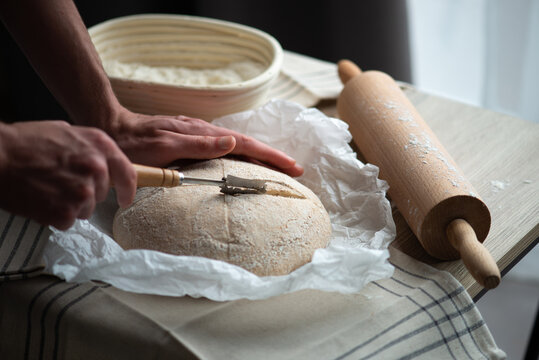 Scoring Sourdough Bread Dough with Bread Lame Before Baking. Traditional homemade bread making process with natural fermentation.