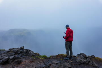 Fototapeta premium Hiker in Red Jacket Standing on Rocky Mountain Peak Iceland
