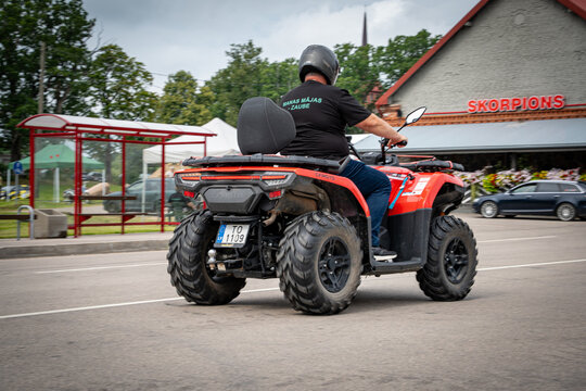 Latvia &ndash; August 2, 2026: Man rides a red CFMOTO ATV through the village center during a public event.