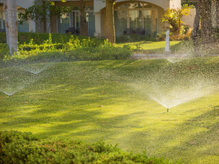 Obraz premium Automatic Irrigation System Watering Lush Green Lawn in Luxury Hotel Resort Garden, Smart Sustainable Water Conservation and Eco Friendly Landscaping Maintenance Concept in Hot Summer Weather