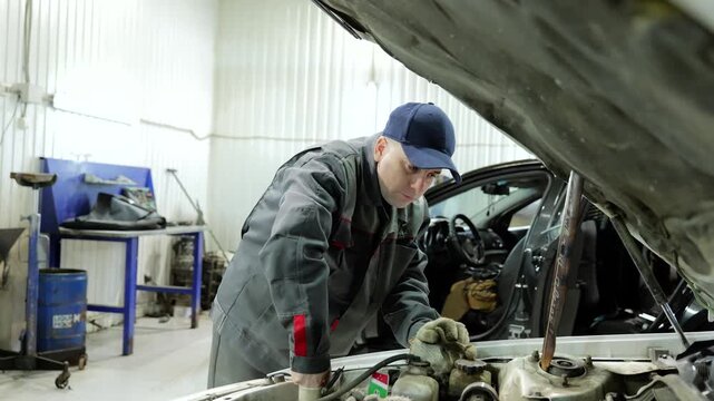 Professional mechanic checking engine compartment, wearing branded uniform, performing diagnostic procedures inside modern automotive service center