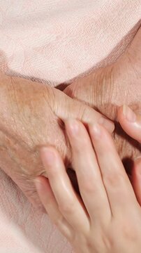 Close up view of a young caregiver tenderly massaging the aged, wrinkled hands of an elderly woman, symbolizing intergenerational support, love, and assistance for seniors