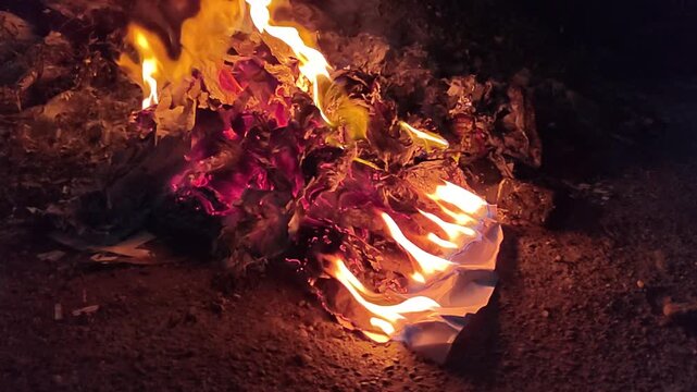 Burning paper and glowing embers in a campfire on the ground at night