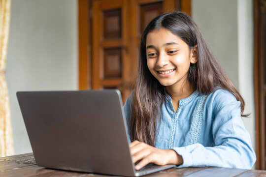 Indian teenage girl smiling and working on laptop at table for remote study background and online learning banner