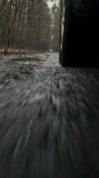 A car's front wheel spins rapidly on a muddy forest road, splashing through deep puddles of liquid mud, as the vehicle's tire treads grip the dirty terrain, navigating the challenging road conditions