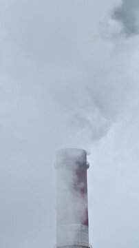 Plumes of thick, dark grey smoke billow from an industrial chimney against a bleak, overcast sky, illustrating the concept of air pollution, fossil fuel emissions, and global warming
