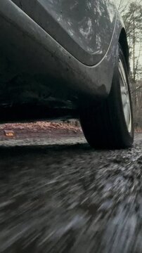 A car's rear wheel spins fast on a muddy forest road, spraying puddles of liquid dirt, the tire grips the slick ground, demonstrating the vehicle's off-road capability in a damp, wooded environment
