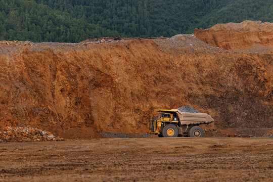 Mining dump truck large open pit quarry with cliff and forest backdrop for industrial banner