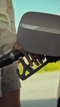 A confident young driver fills her car with gasoline on a sunny day, firmly grasping the fuel nozzle, performing a routine yet essential task of refueling her vehicle independently