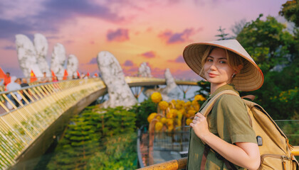 Fototapeta premium Young caucasian female tourist at golden bridge in ba na hills, Da nang, Vietnam during sunset