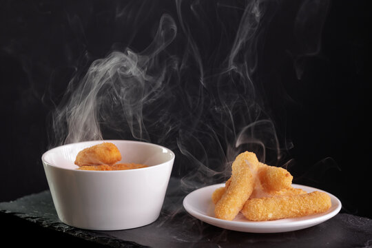 Hot crispy fish fingers in white bowls against black background