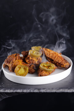 Closeup Spicy fried chicken wings with jalapenos on smoky white plate