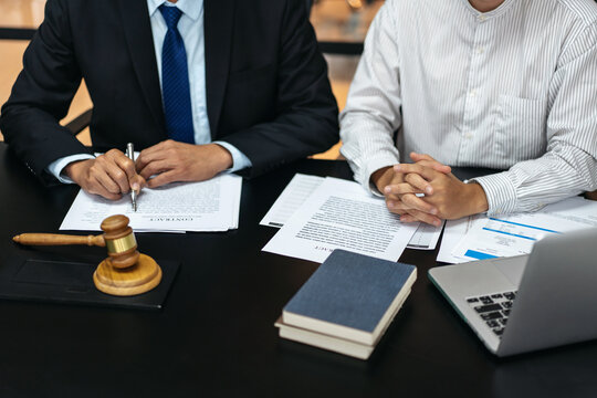 Two men in suits are sitting at a table with papers and a gavel