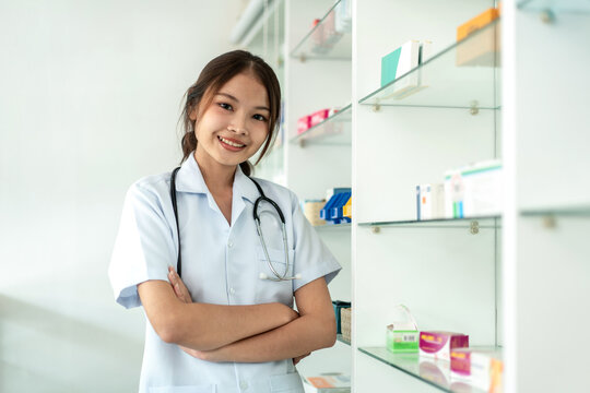 A woman in a white coat stands in front of a pharmacy shelf