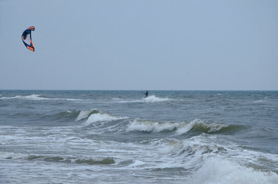 Kitesurfer riding the waves under a clear sky with a colorful kite soaring high above the choppy sea. Active recreation by the sea , vacation by the ocean, a trip to the sea, hobbies and sports.