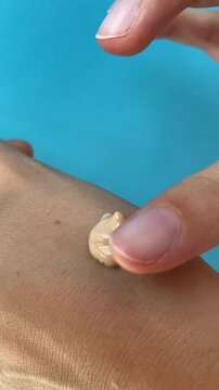 Close up of female hands spreading applying liquid foundation on hand, make up routine. Creating a makeup swatch on blue background. Foundation application content, vertical lifestyle UGC content