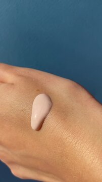 Close up of female hands spreading applying liquid foundation on hand, make up routine. Creating a makeup swatch on blue background. Foundation application content, vertical lifestyle UGC content