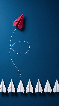 Red paper airplane takes flight from a row of white ones, symbolizing leadership, innovation, and breaking free from the norm