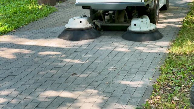 Street sweeper machine cleaning a paved sidewalk in a park