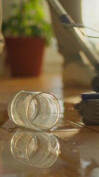 A person mops a hardwood floor in a bright room, while several cups lie overturned, spilling their contents onto the floor, a bucket with cleaning supplies sits nearby, part of the cleaning task