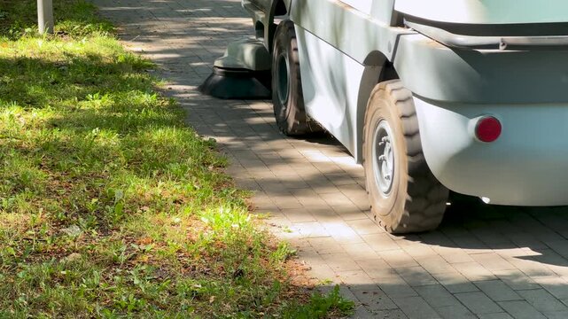 Street sweeper machine cleaning a paved sidewalk in a park