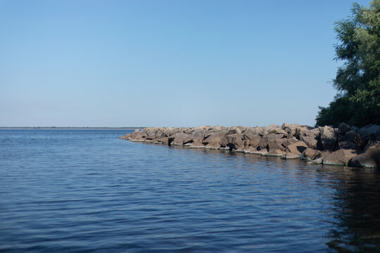 Peaceful summer lake with rocky shoreline, green trees and wide blue sky copy space