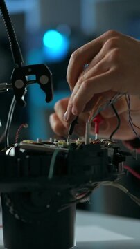 An engineer at a lab bench assembles a robotic device, routing wires and fastening components, focusing on precise circuitry integration during a detailed technical assembly process