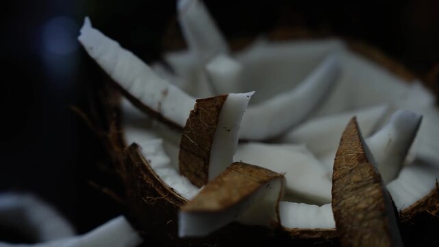 Close-up of fresh coconut pieces in shell on a dark background, showing white flesh and brown husk with a natural rustic look