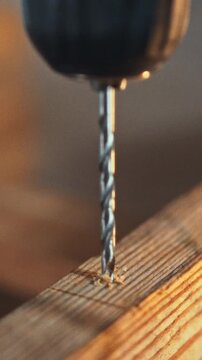 Carpenter in bustling workshop drills precise hole into piece of wooden material with an electric drill, performing a woodworking task that requires accuracy and skill, amid the sounds of other tools