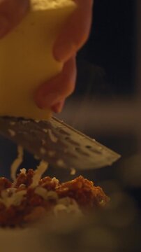 Chef, the person preparing the meal, grates cheese onto plate of pasta covered in a rich meat sauce, the chef's hand holding a grater, soft lighting in the kitchen, a warm, inviting dinner atmosphere