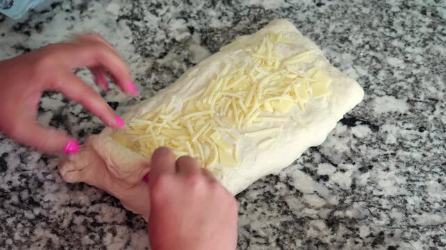 Baker stretch-and-folding sourdough dough, incorporating cheese, resting on granite countertop before baking into a golden, artisanal loaf of bread