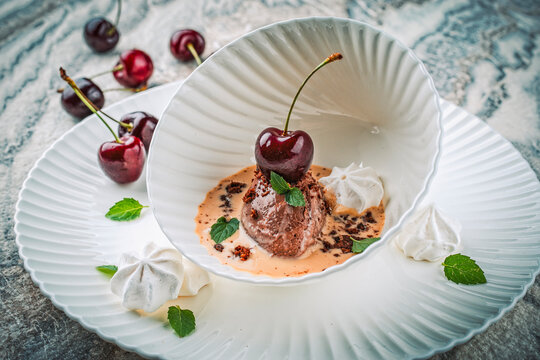 Modern dessert - dark black chocolate mousse au chocolat in vanilla sauce with black sweet cherries and meringues served as close-up in a design bowl