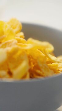 In a kitchen, a dieter assembles breakfast, pouring cornflakes onto a white plate while milk is set beside it, yellow kernels cascade in slow motion, low-calorie start to the day today