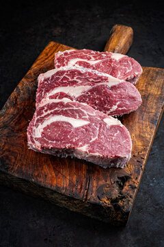 Dry aged meat raw beef entrecote cuts with fat marbling offered as close-up on a rustic wooden cutting board