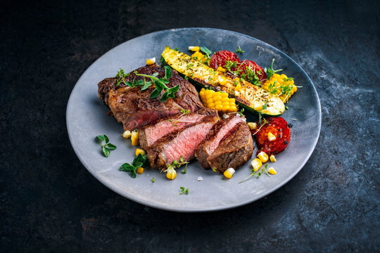 Dry aged roasted beef entrecote with grilled vegetables, zucchini, sweet corn and greens served as close-up on a design plate