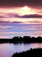Fototapeta premium Dramatic sunset sky over city skyline reflection on water background with pink and purple clouds twilight urban view dusk landscape