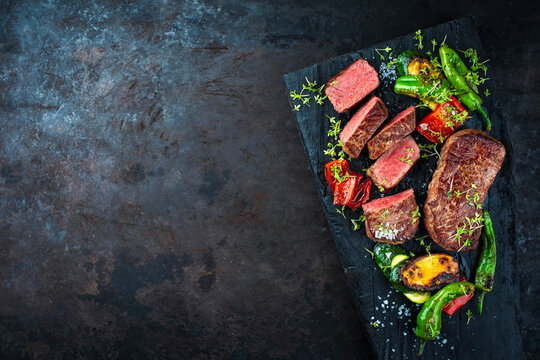 BBQ broiled gry aged roastbeef with roasted vegetabled served as top view on rustic wooden board with copy space left