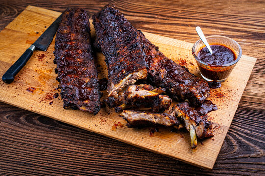 Barbecue spare ribs St Louis baby back cut with homemade artisan hot chili bbq grill sauce dip served as close-up on a wooden baord