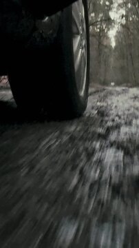 Rear wheel of a vehicle spins rapidly, throwing mud puddles onto a forest road as it drives through wet terrain, the wheelbase and axle turning together, off-road motion in challenging conditions