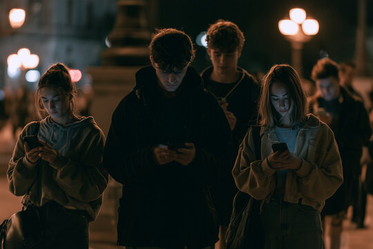 Young people using smartphones at night, illuminated by screens, representing digital connection and screen addiction
