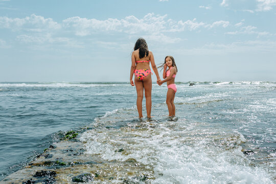 Two Sisters Holding Hands Walking towards the Sea, smaller sister looking at camera