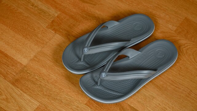 Tambov, Russian Federation - July 25, 2026 A pair of gray Crocs Crocband flip-flops on a parquet floor