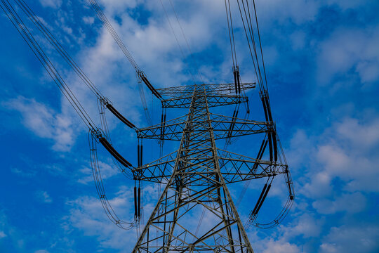 High voltage transmission tower, power pylon against cloudy blue sky