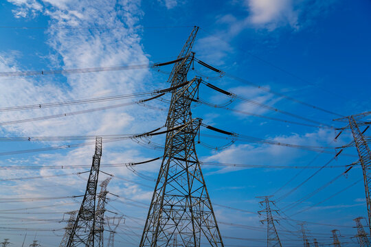 High voltage transmission tower, power pylon against cloudy blue sky