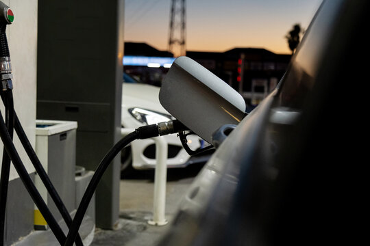 Fuel nozzle at oil station with car at sunset