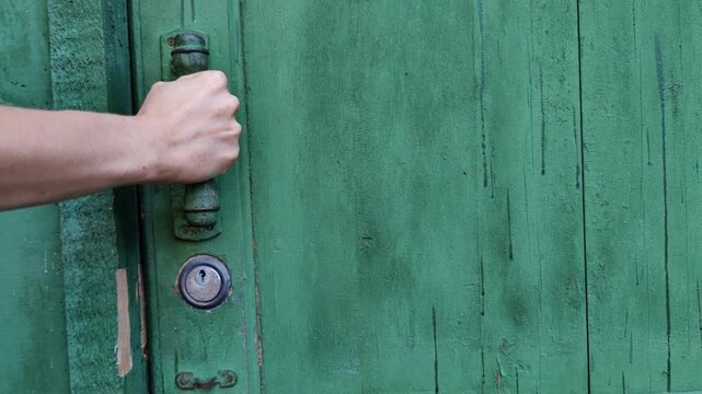 woman pulls the handle to open a weathered green wooden gate after unlocking it, property access, rustic entrance, home security.