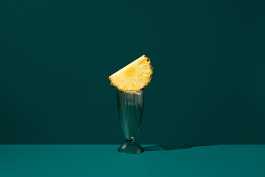 Pineapple slice on glass against dark teal background