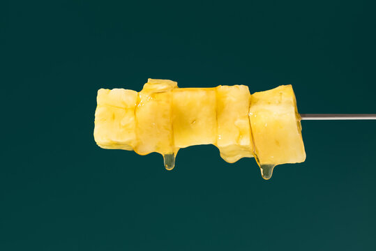 Pineapple skewer with syrup against dark green background