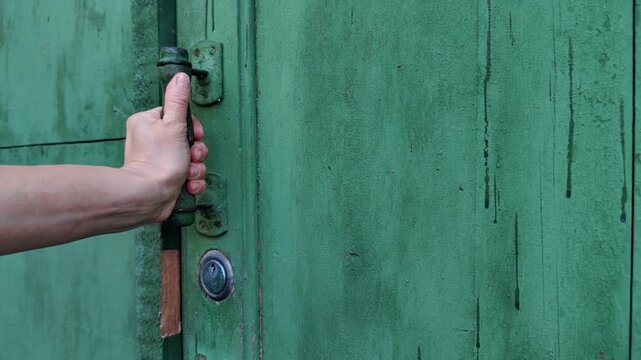 woman opens a weathered green wooden gate by pulling the metal handle, rustic entrance, residential access, property security, outdoor setting.