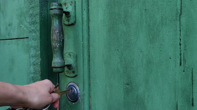 woman reaches for the lock on a weathered green wooden gate while holding the handle, home security, rustic entrance, access control.